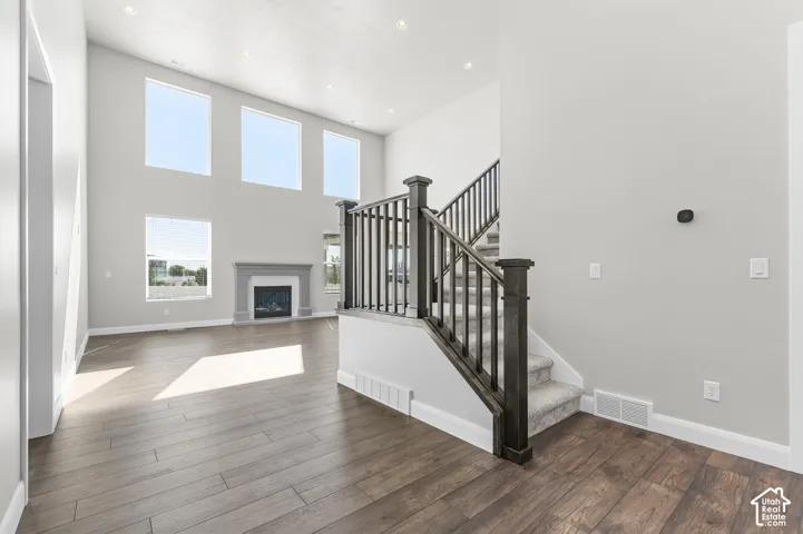 Vaulted ceilings, expansive windows, fireplace with stone-finish surround, wood-finish flooring, and staircase with dark-stained railing