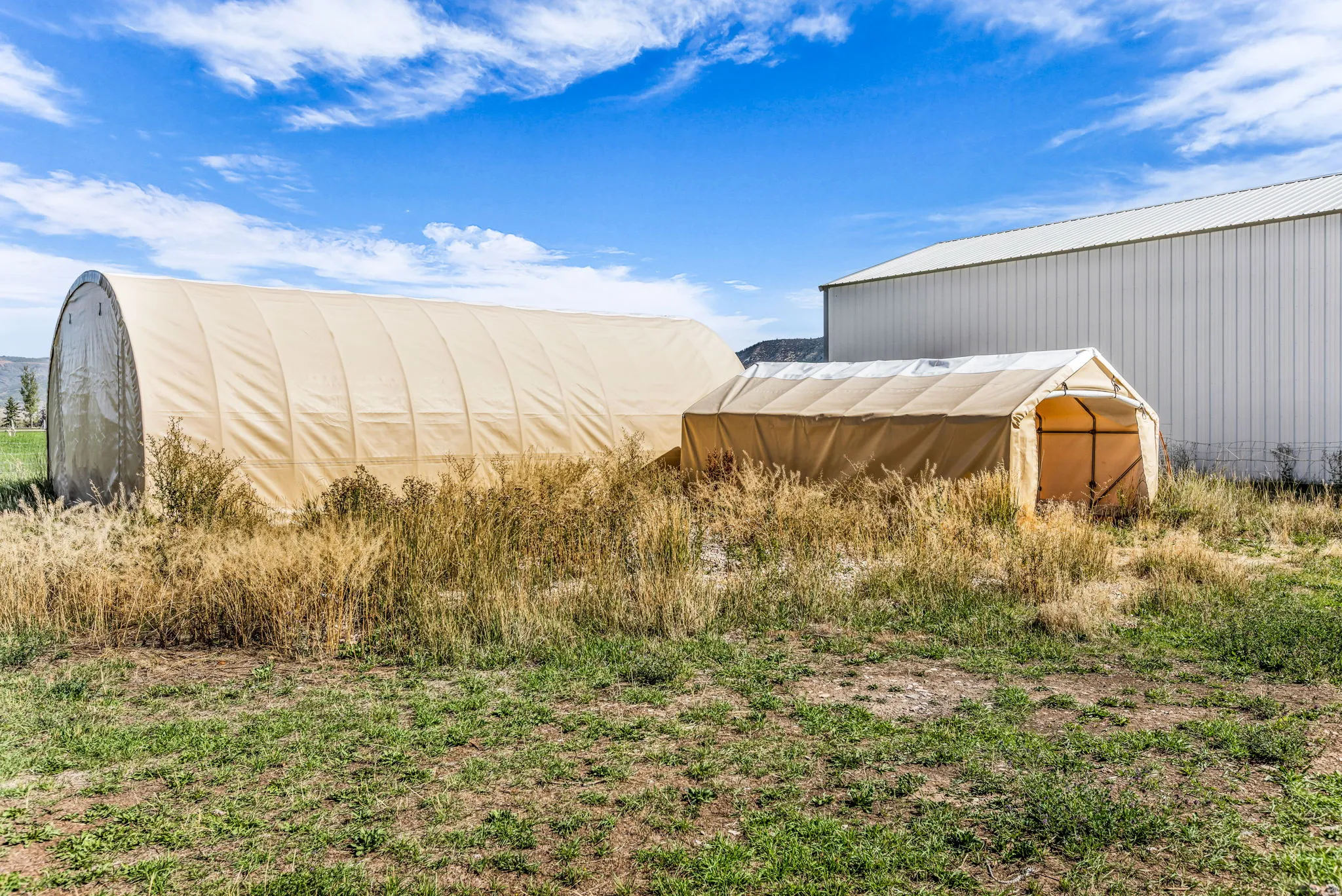 Two canvas-covered structures on a grassy lot perfect for storing vehicles, boat, or four-wheelers.