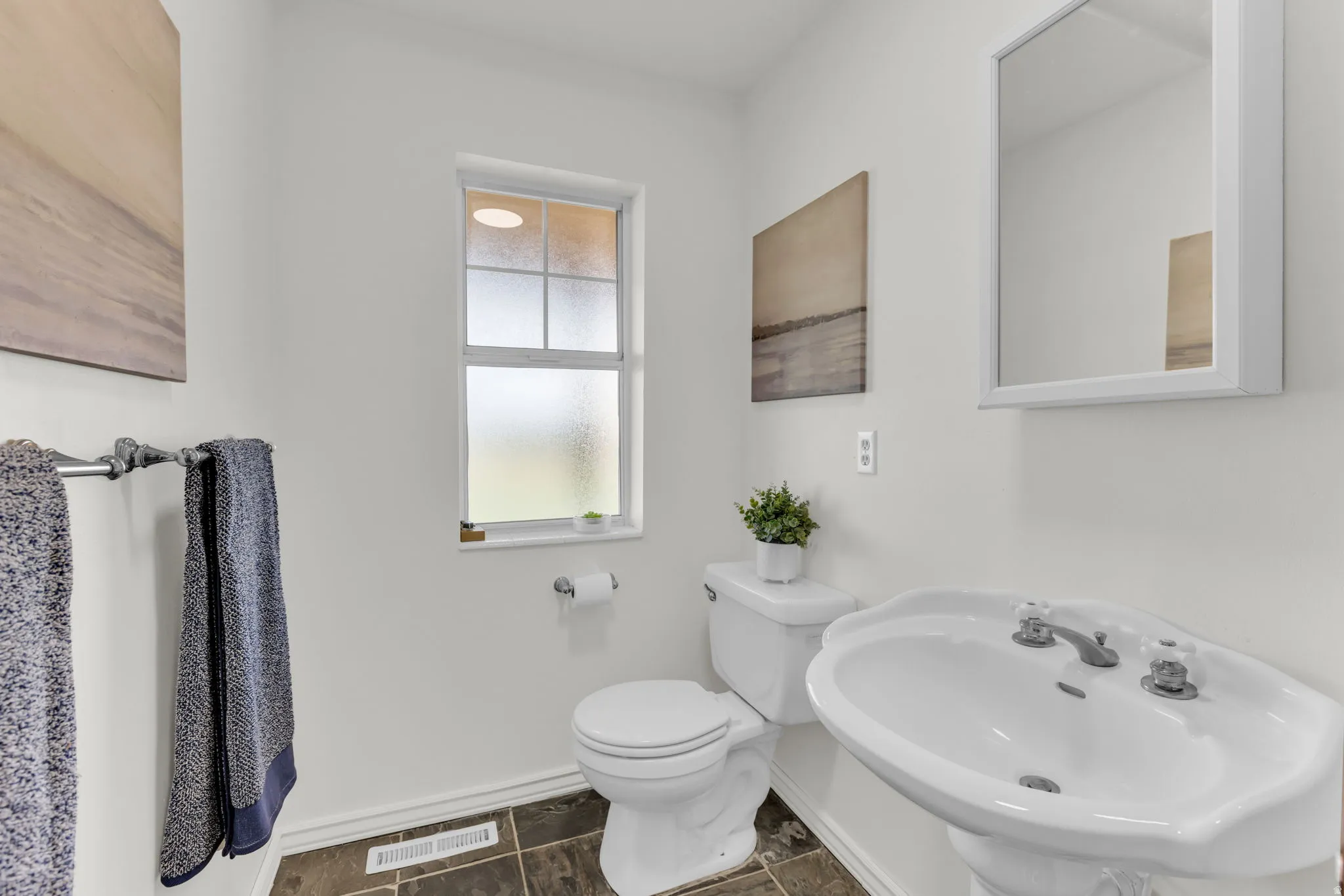 Half bath with white pedestal sink, wall-mounted mirror, and a window with frosted glass