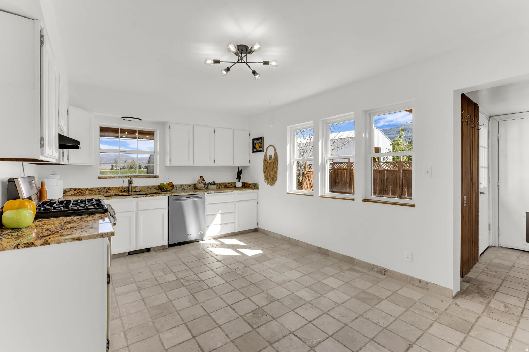 Kitchen with white cabinetry, stainless steel dishwasher, stone countertops, and tile flooring