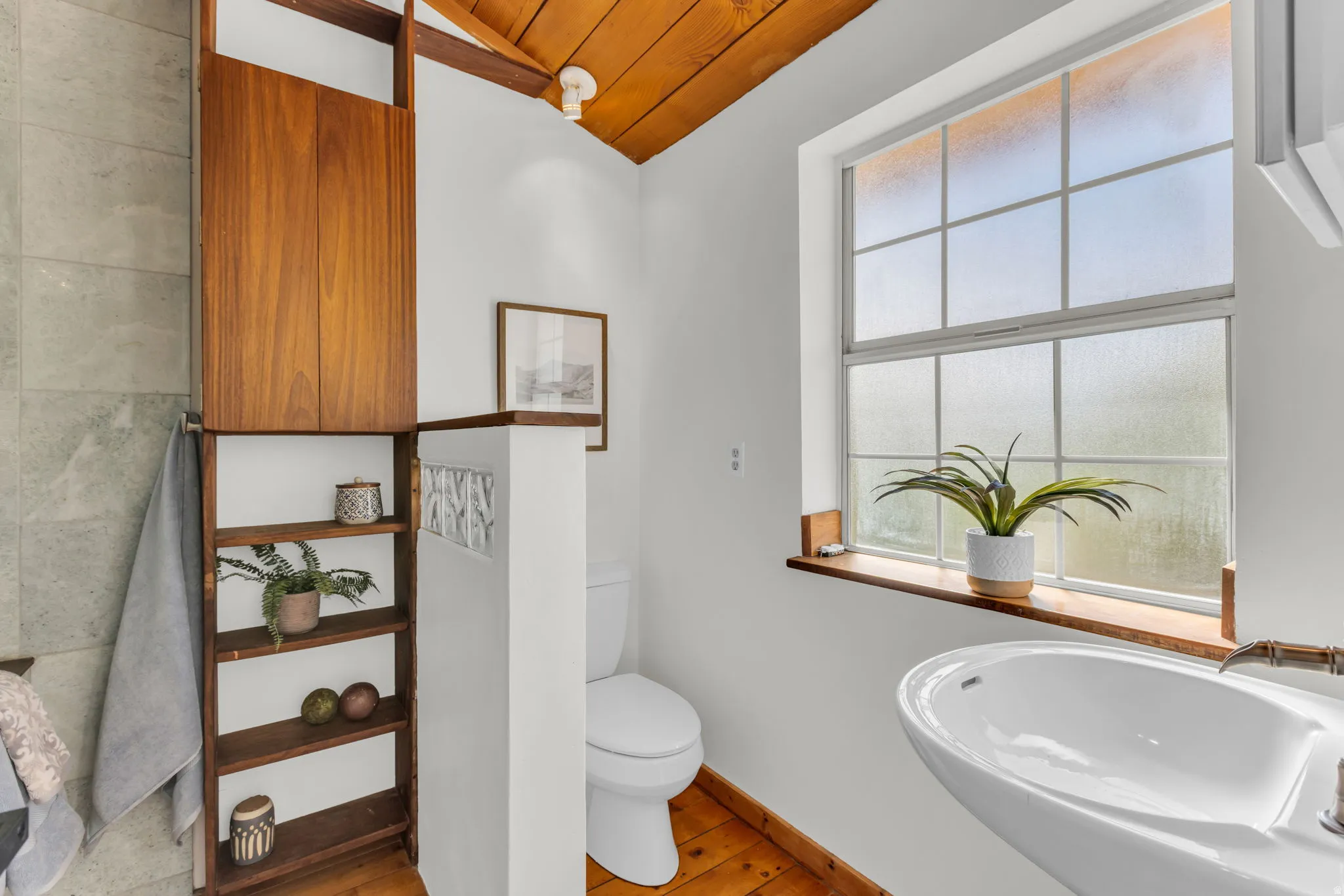 Primary bathroom with vaulted wood ceiling, wood flooring, built-in open shelving, built-in closed cabinetry, and a pedestal sink