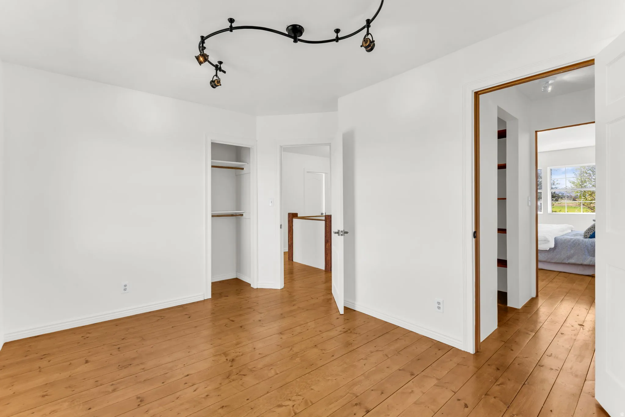 Hardwood flooring, track lighting fixture, open doorway, built-in closet, white walls