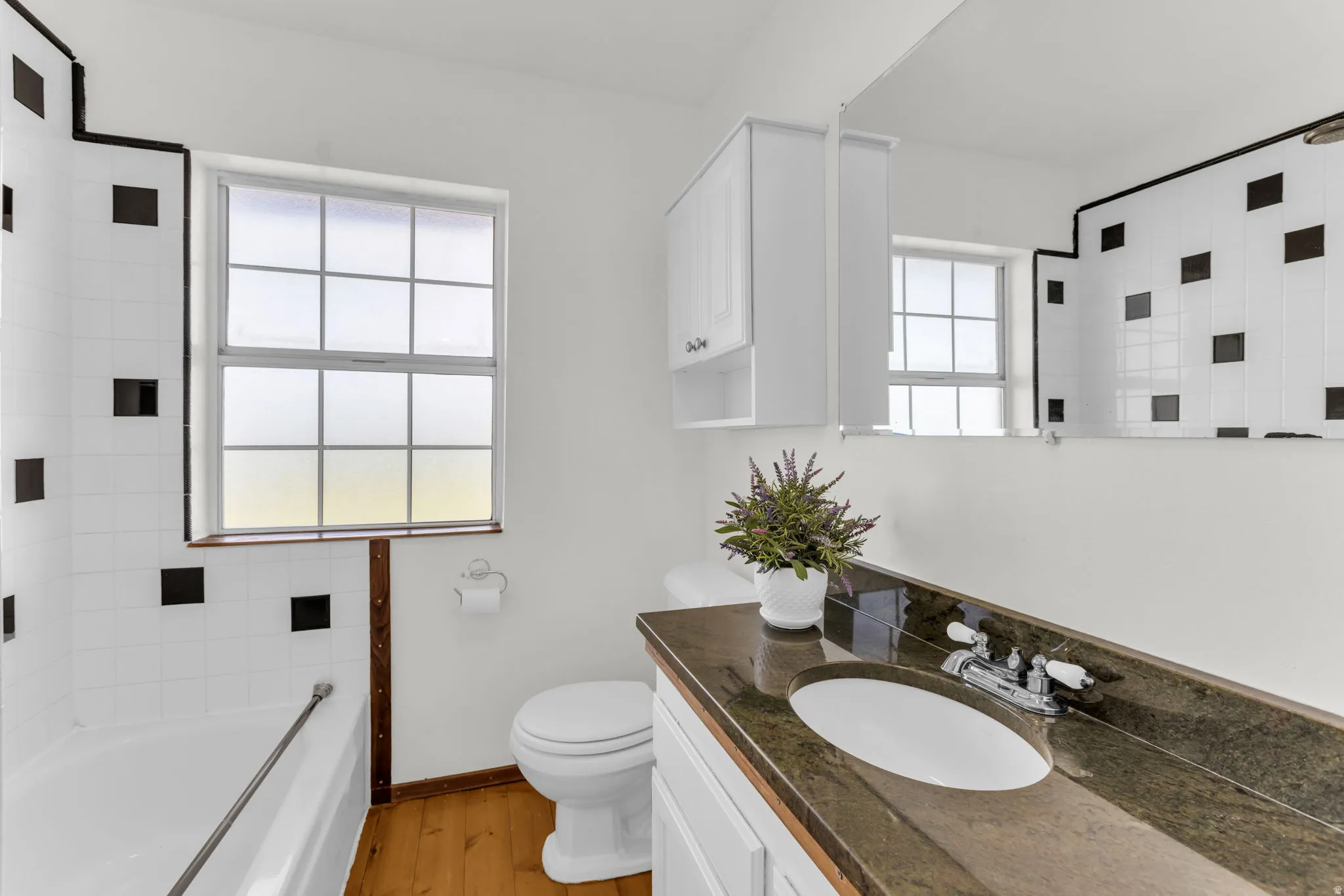Windowed full bathroom featuring a built-in tub, white vanity with an undermount sink, stone countertop, and upper cabinetry