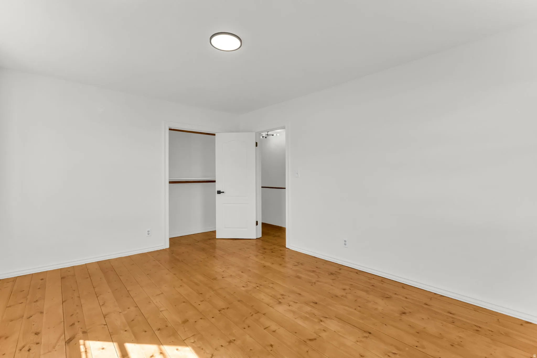 Light wood flooring, white walls, flush-mount ceiling light fixture, and two closet openings with hanging rods
