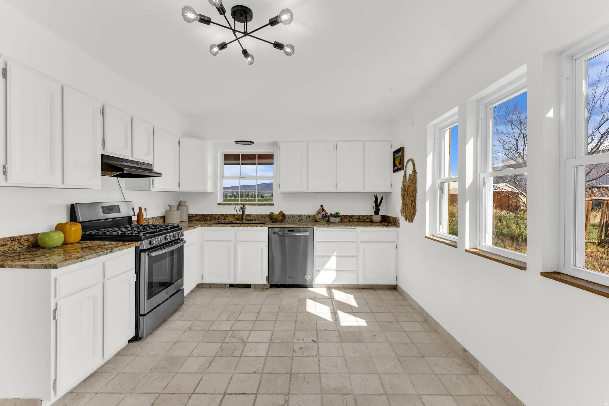 White cabinetry with dark contrasting hardware, stone-finish countertops, stainless steel appliances, and a modern ceiling light fixture