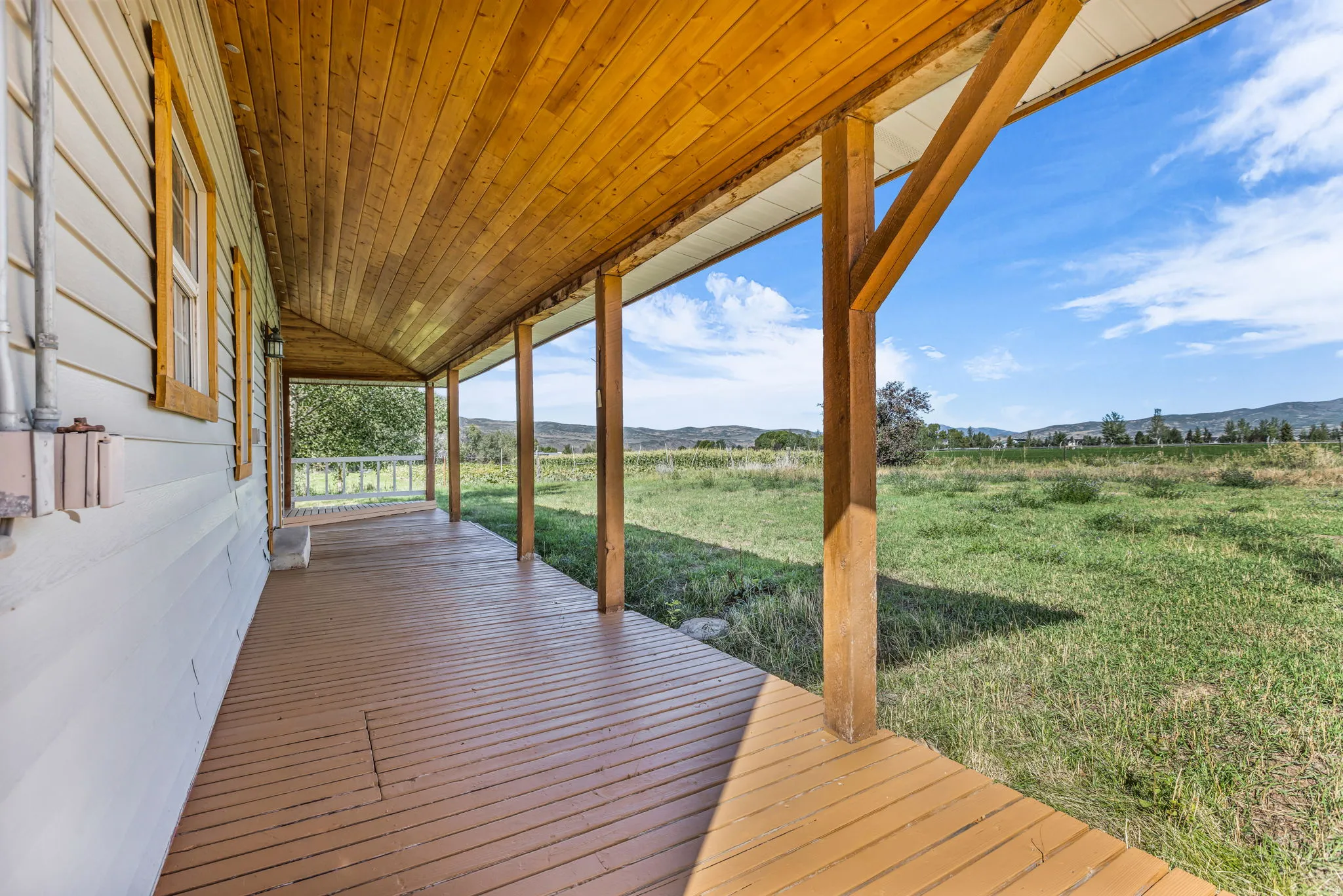 Covered porch with wood ceiling, wood-frame windows, and brown decking
