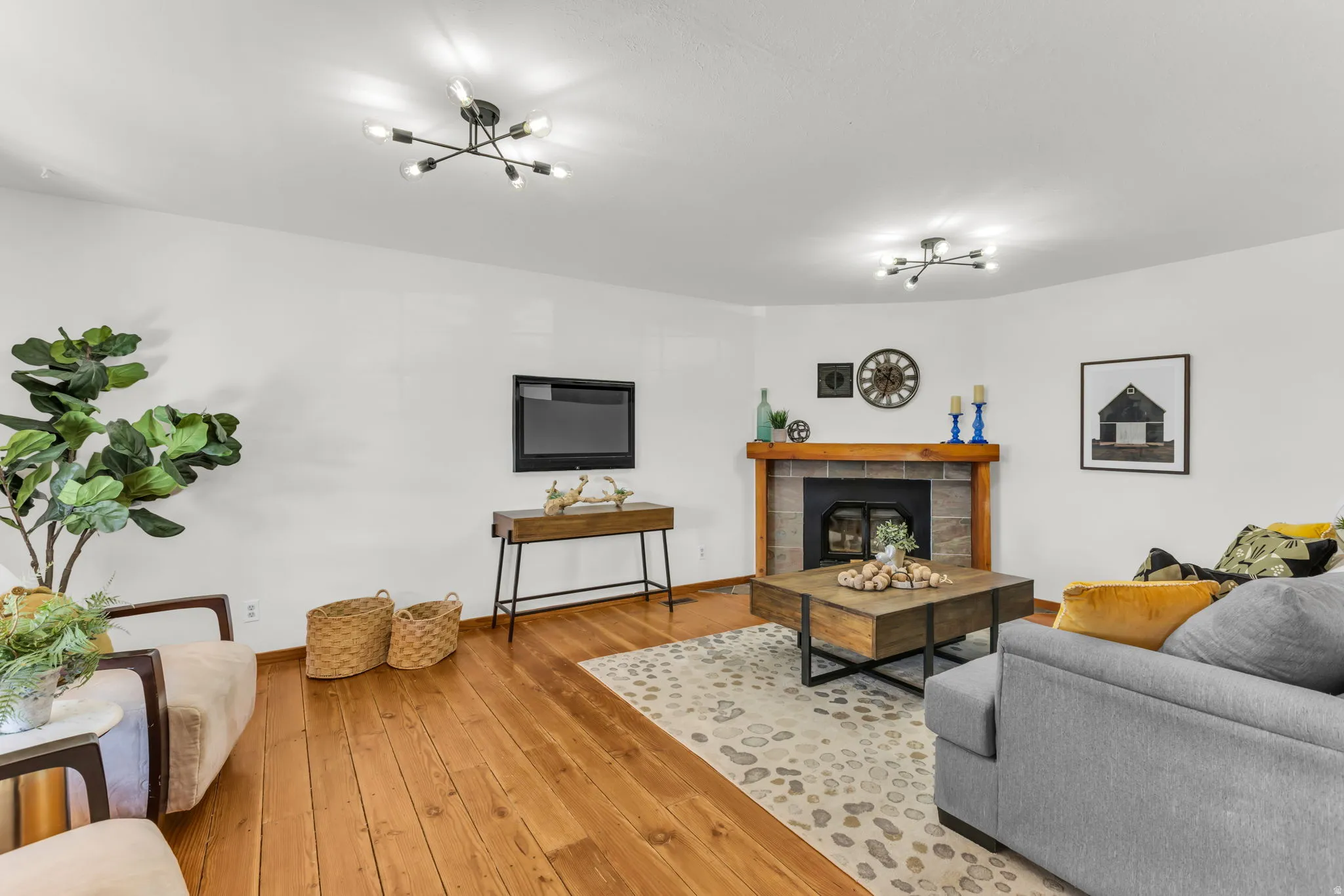 Hardwood flooring, stone-clad fireplace with wood mantle, modern flush-mount lighting, and white wall finishes