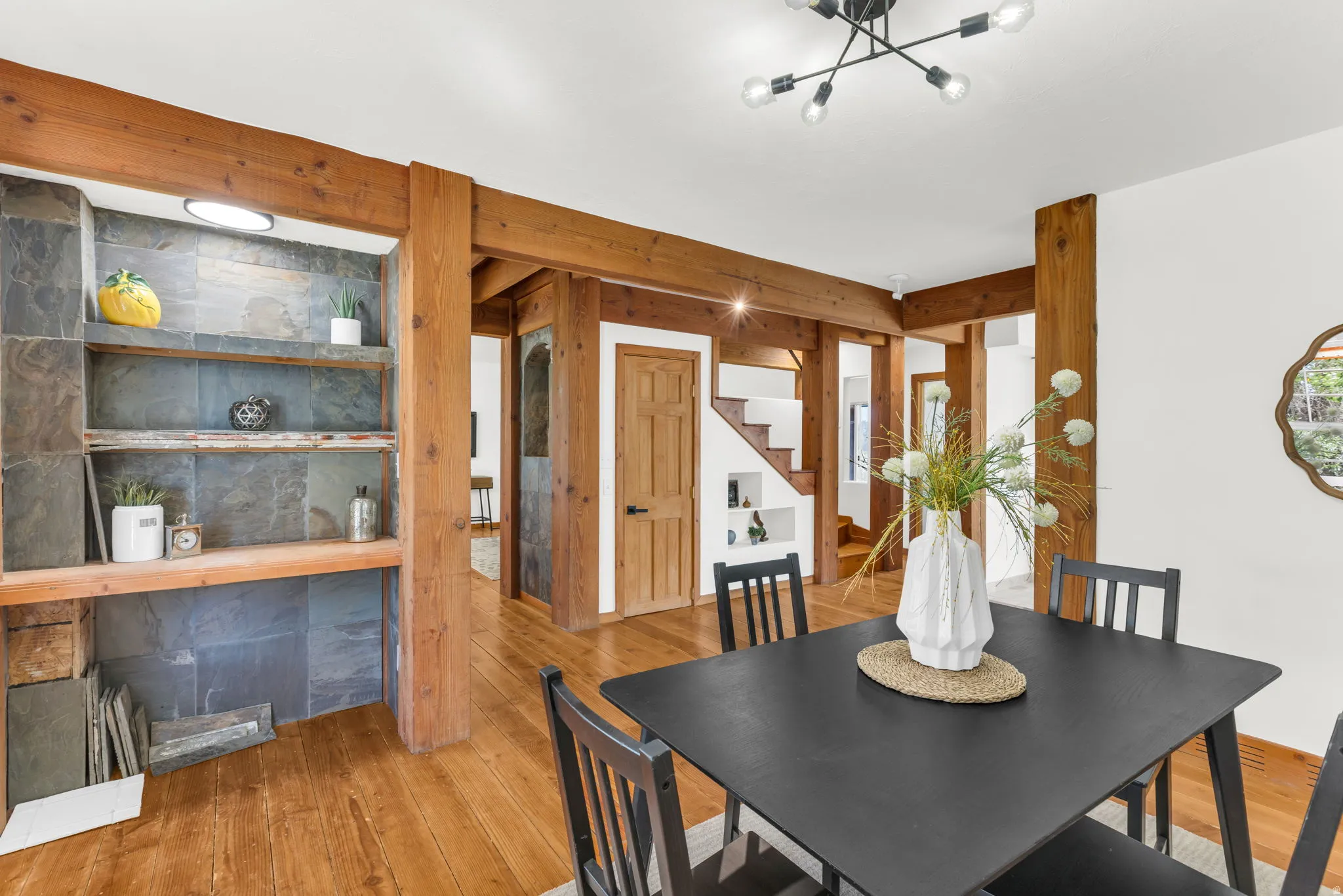 Exposed wood beams and columns, wood-finish flooring, built-in shelving with stone-finish backing, and a modern ceiling light fixture