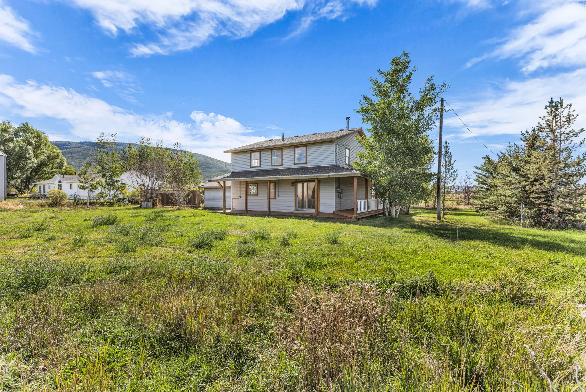 Two-story residence with a covered wrap-around porch, multiple windows, and a light-colored exterior