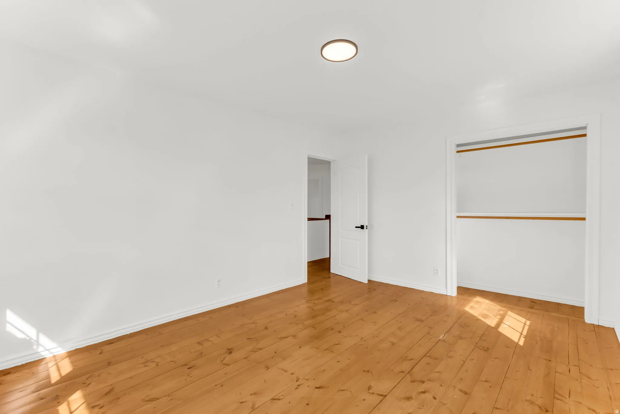 Wood flooring, white painted walls, a flush-mount ceiling light, a built-in closet, and a white interior door with dark hardware
