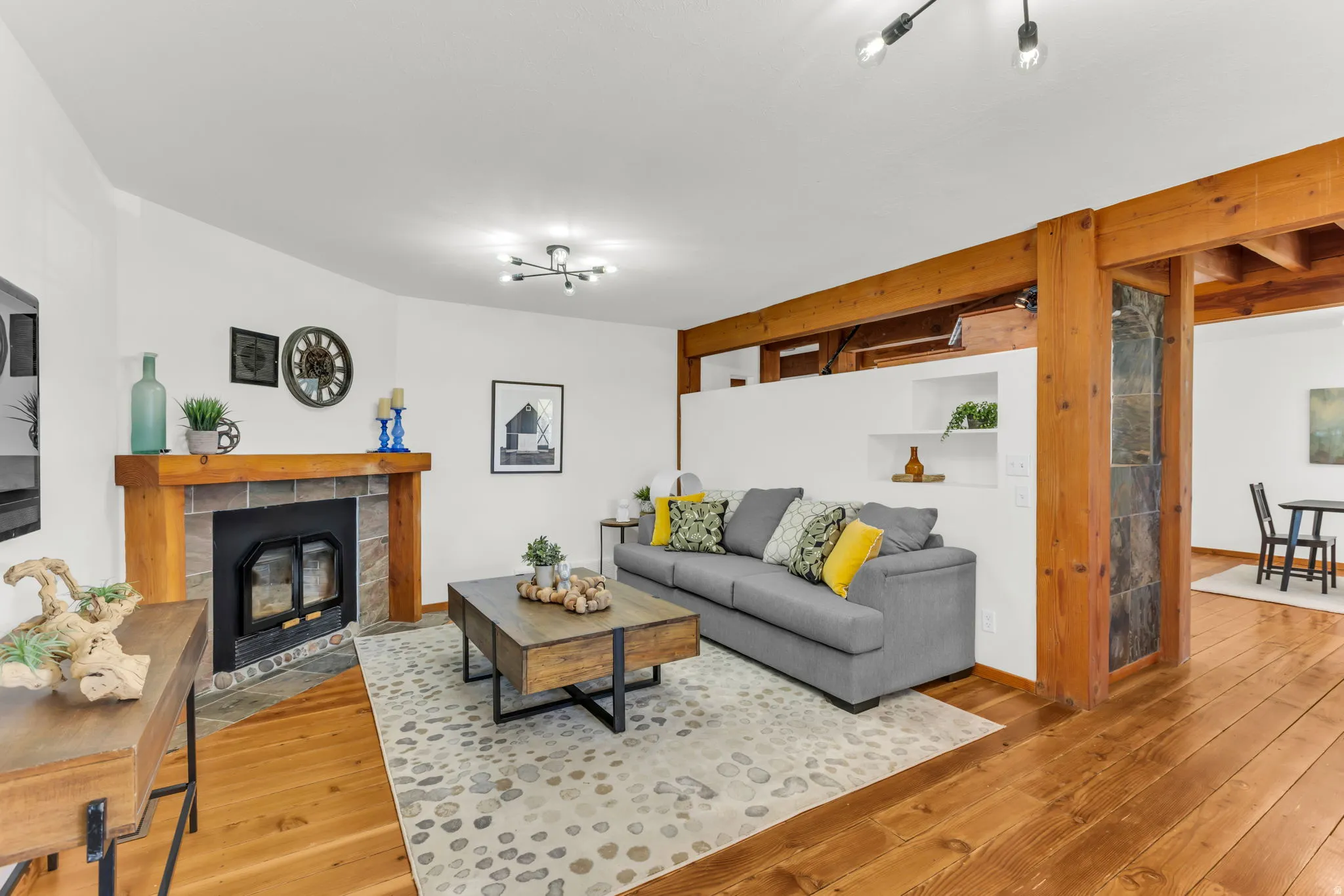 Living area featuring a stone-faced fireplace with a wood mantle, wood-finish flooring, exposed wood beams, and a built-in wall niche