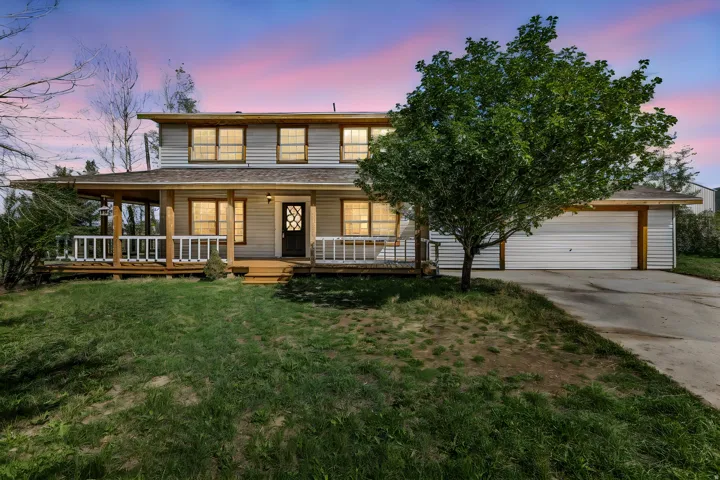 Two-story residence featuring siding exterior, wood-tone front porch with white railing, and an attached two-car garage