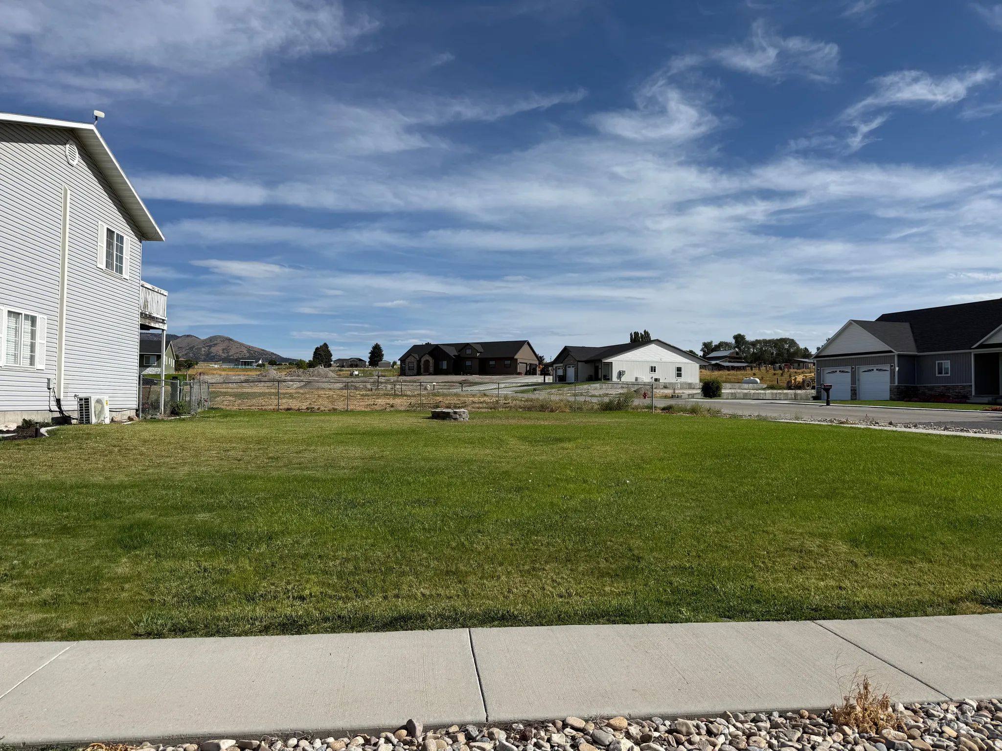 Expansive lot featuring a level, grassy area, paved sidewalk, and decorative rock border