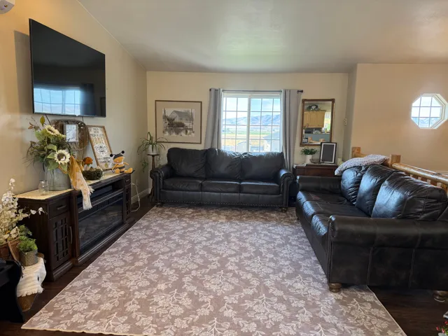 Warm neutral wall paint, wood-finish flooring, built-in electric fireplace, octagonal window, and a large picture window