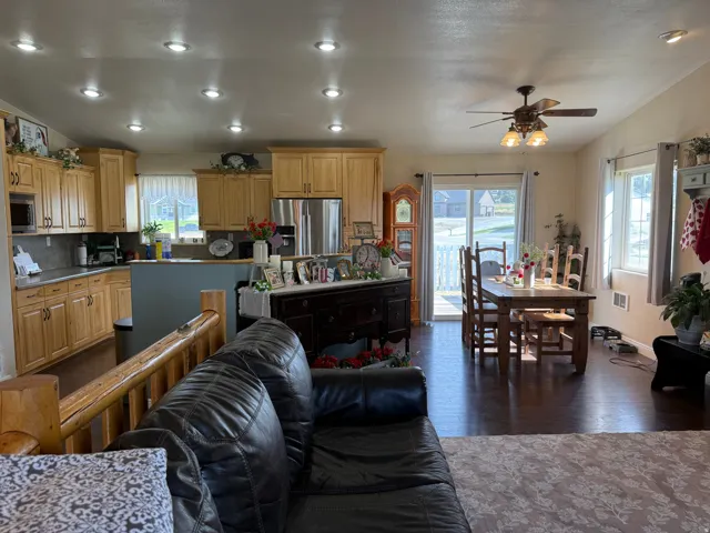 Recessed ceiling lighting, wood-finish flooring, kitchen with light wood cabinetry, stainless steel appliances, and a ceiling fan in the dining area