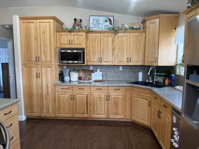 Wood-finish flooring, light wood cabinetry, stainless steel microwave, black sink fixture, and a tile backsplash