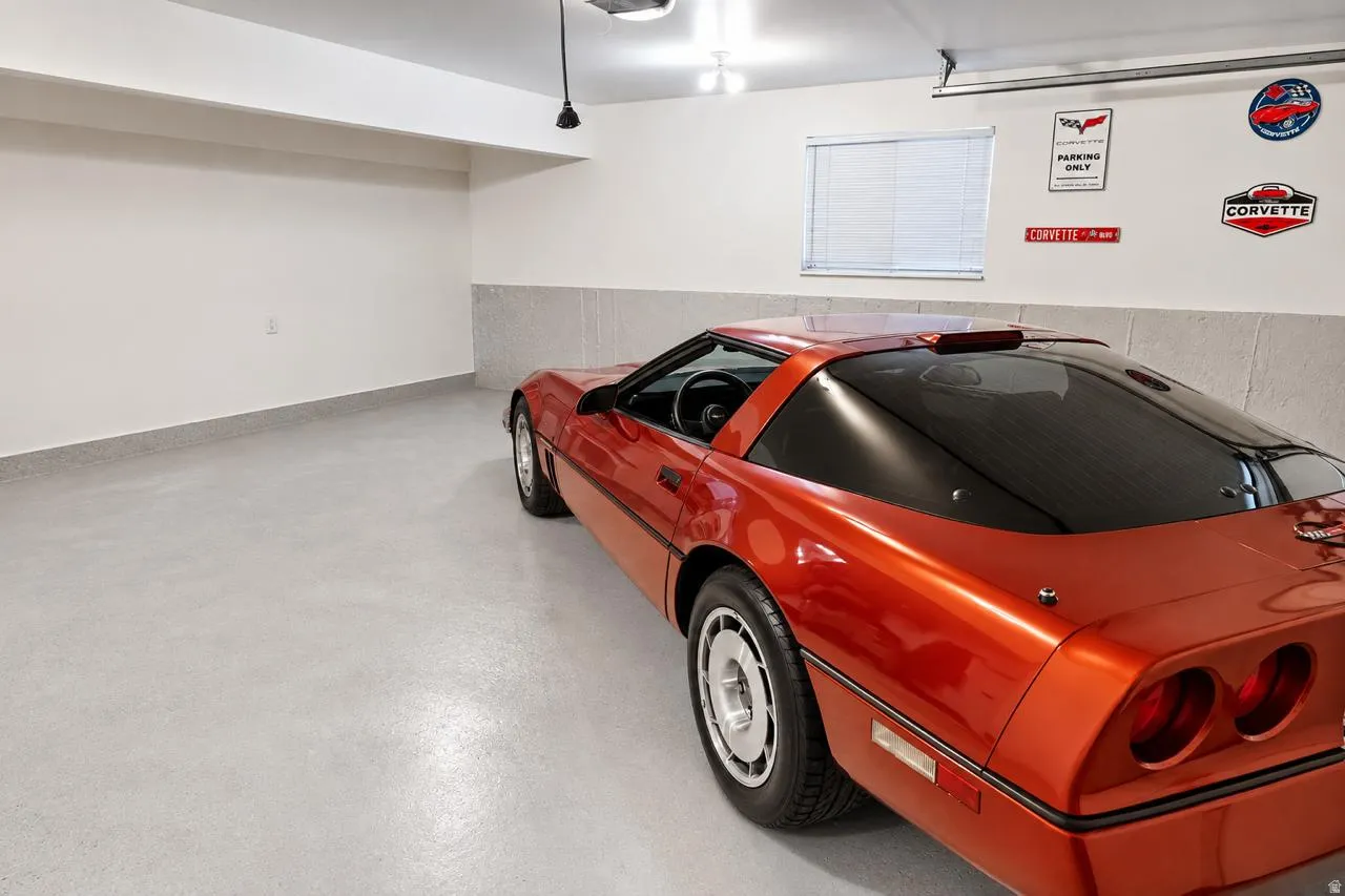 Garage featuring a light-colored epoxy floor, clean white walls, a single window with blinds, and overhead lighting