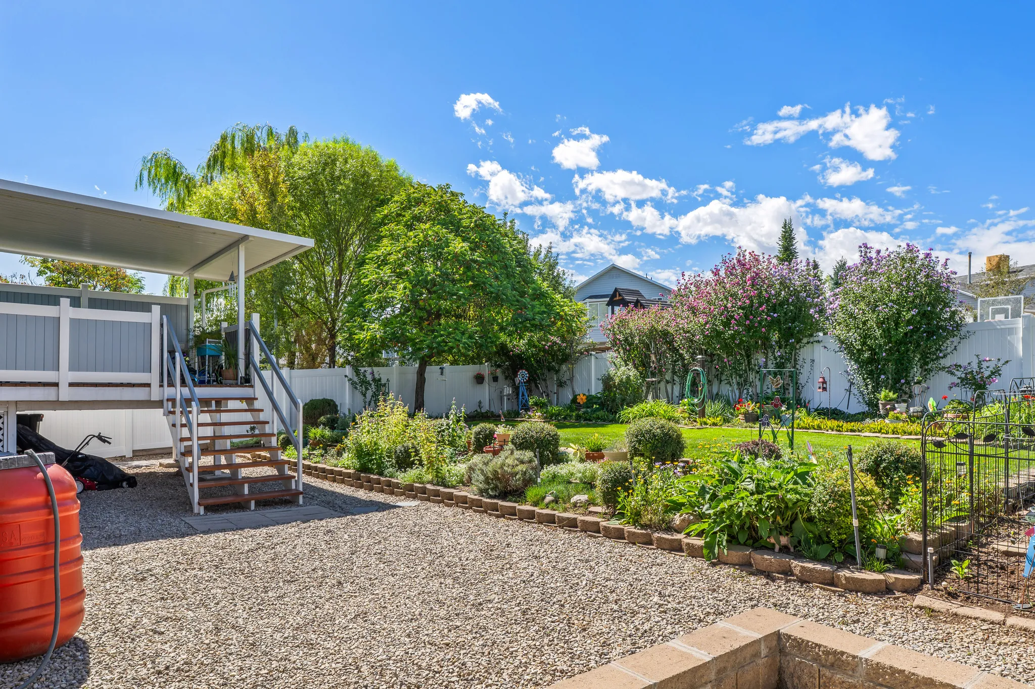 Expansive gravel patio with a covered deck, exterior stairs, and a brick-lined garden bed
