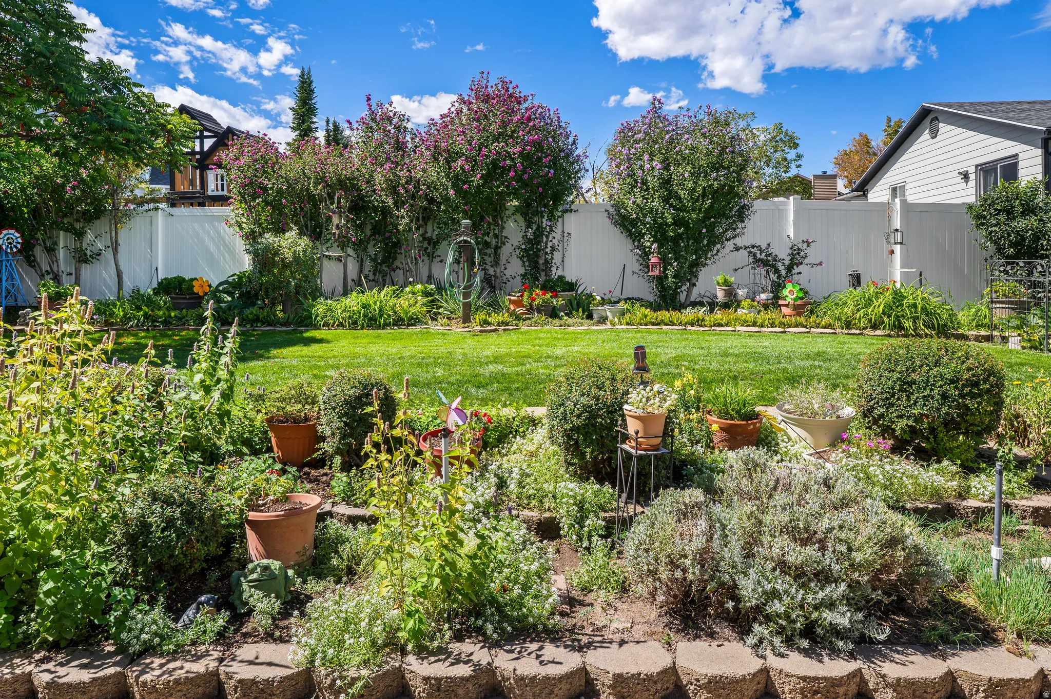 Expansive backyard featuring a lush lawn, mature trees, and a tiered garden bed with stone retaining walls