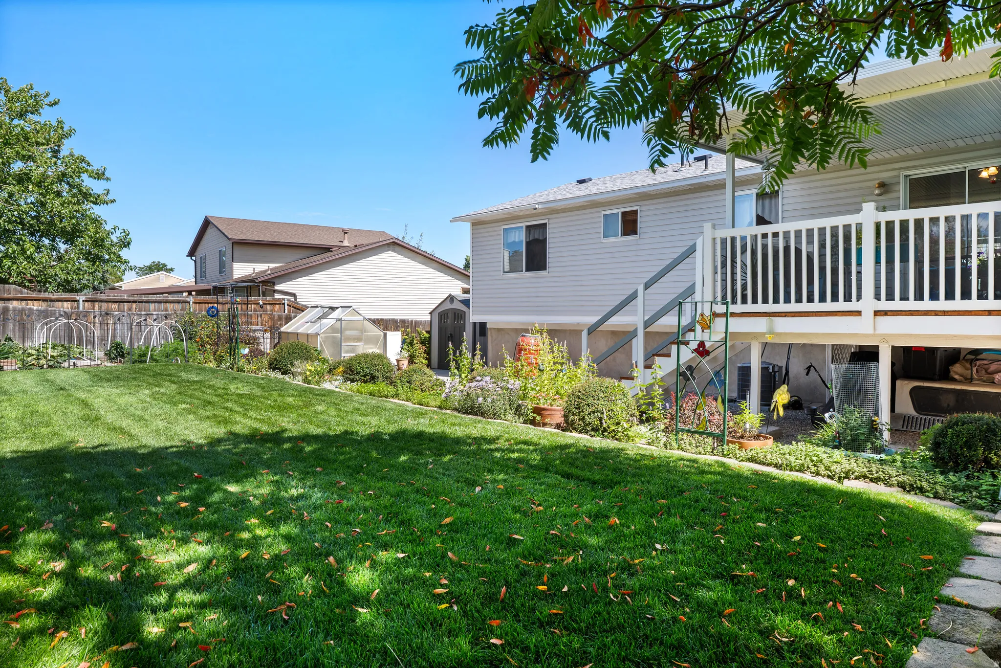 Spacious backyard featuring a manicured lawn, established landscaping, and a greenhouse structure