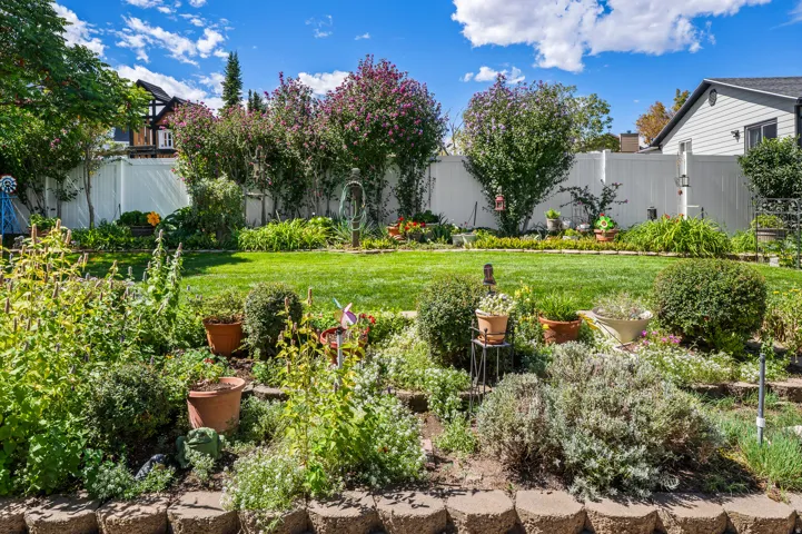 Expansive backyard featuring a lush lawn, mature trees, and a tiered garden bed with stone retaining walls