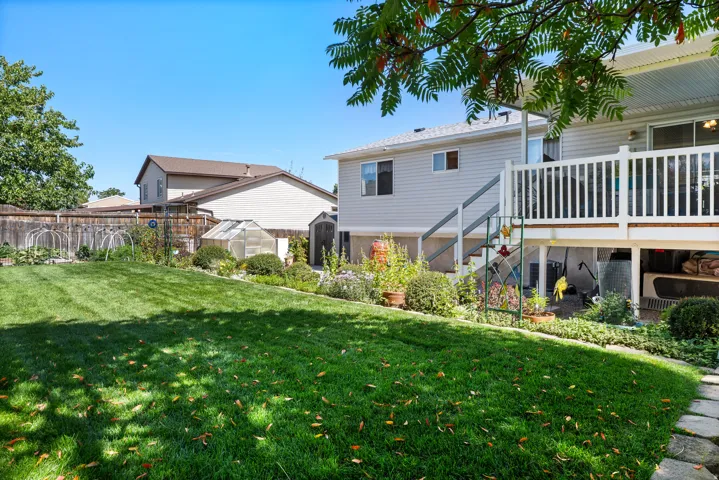 Spacious backyard featuring a manicured lawn, established landscaping, and a greenhouse structure