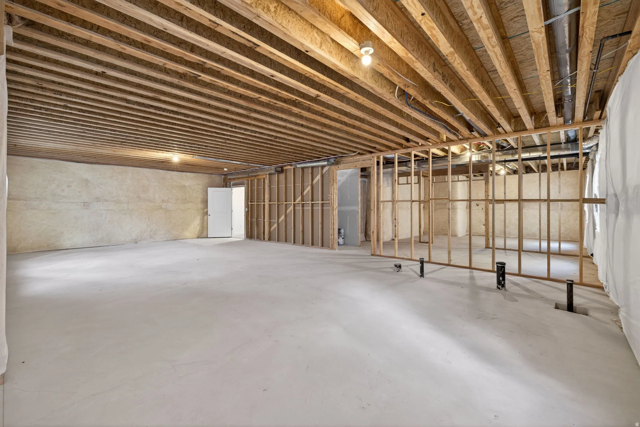 Unfinished basement with exposed wood joists, concrete flooring, and partial wood framing for future development