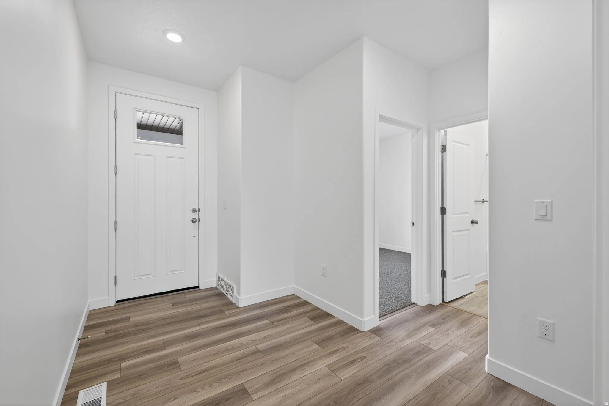 Entryway featuring wood-finish flooring, recessed lighting, white interior doors, and a white front door with a transom window