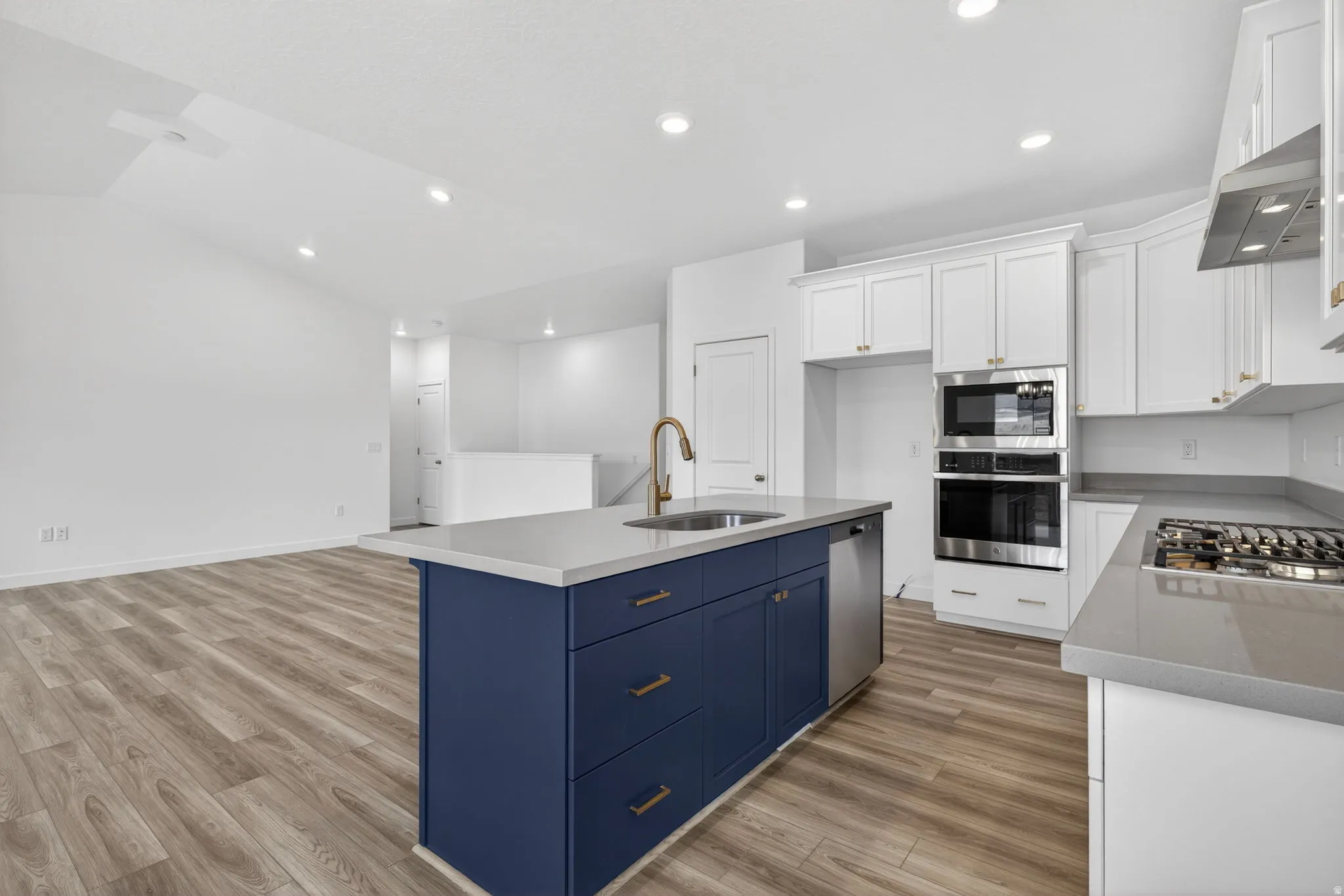 Kitchen featuring a blue island with integrated sink, stainless steel appliances including a wall oven and microwave, white cabinetry, and wood-finish flooring