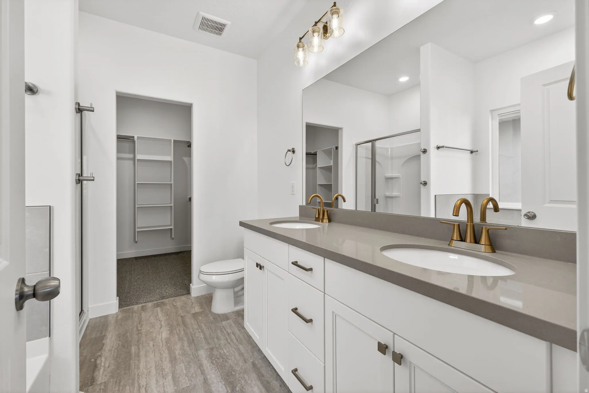 Dual vanity with white cabinetry, gold-finish fixtures, a large mirror, and wood-finish flooring
