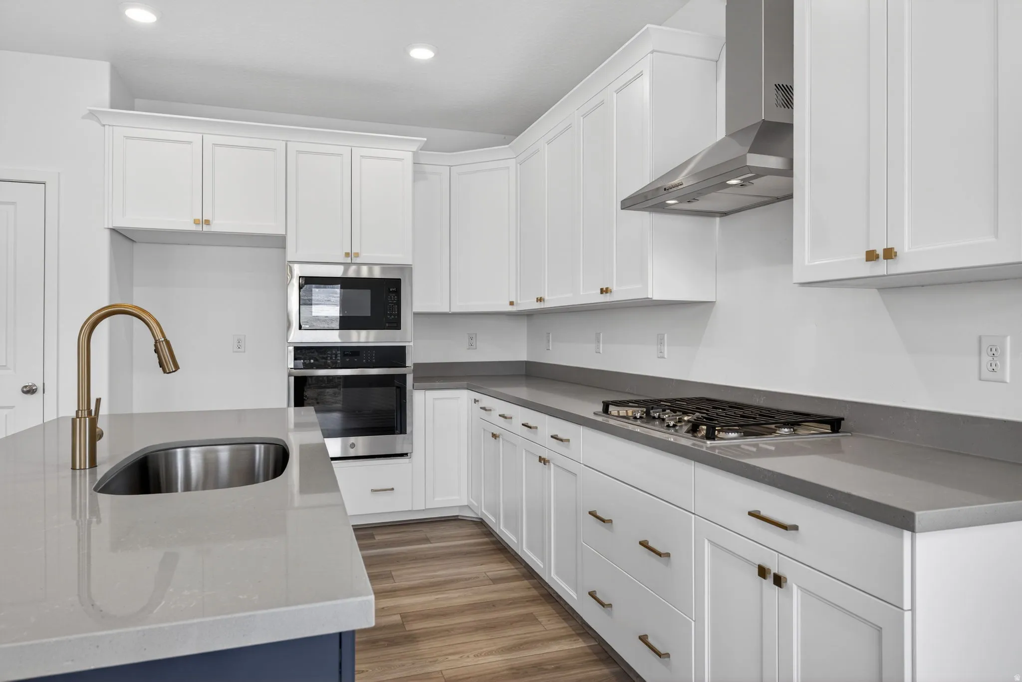 White cabinetry with gold-tone hardware, stainless steel appliances, solid surface countertops, and wood-finish flooring