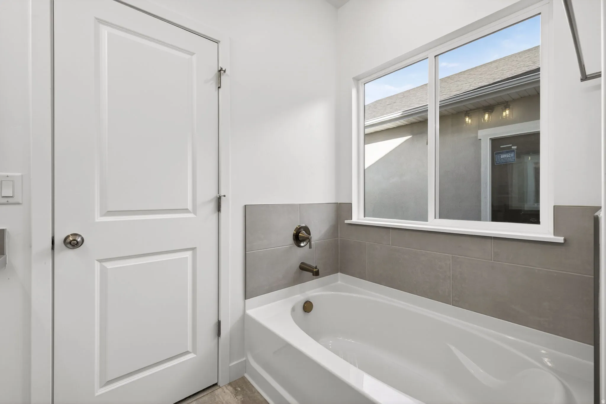 Bathtub with gray tiled surround, bronze-finish fixtures, and a large window
