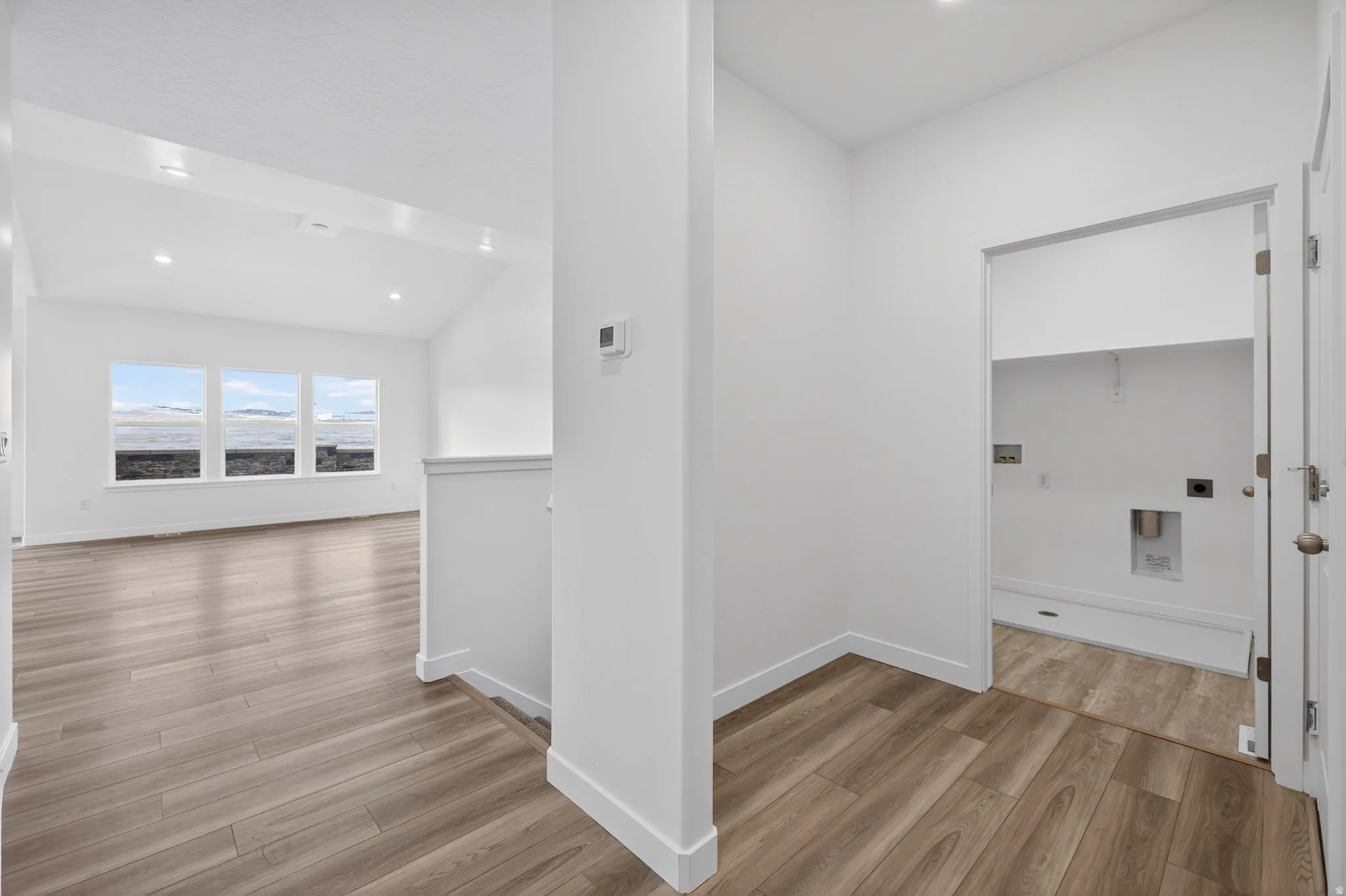 Vaulted ceiling with recessed lighting, wood-finish flooring, multiple windows, and a dedicated laundry area