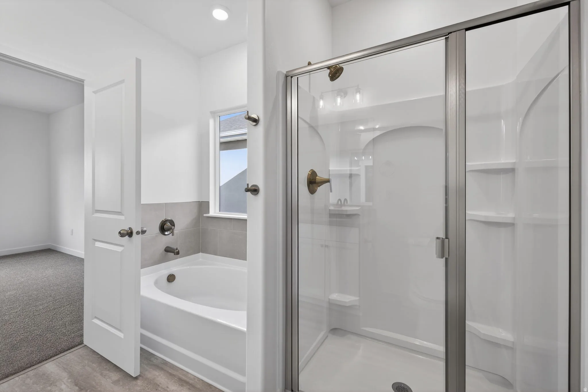 Bathtub and shower combination featuring a glass enclosure, tiled surround, and brushed bronze fixtures