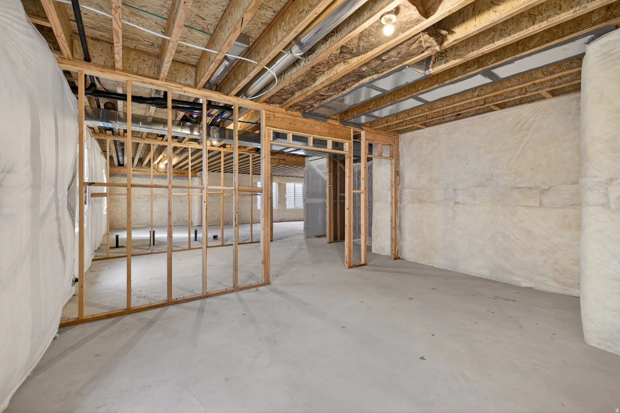 Unfinished basement with concrete flooring, exposed wood framing, and visible ceiling joists