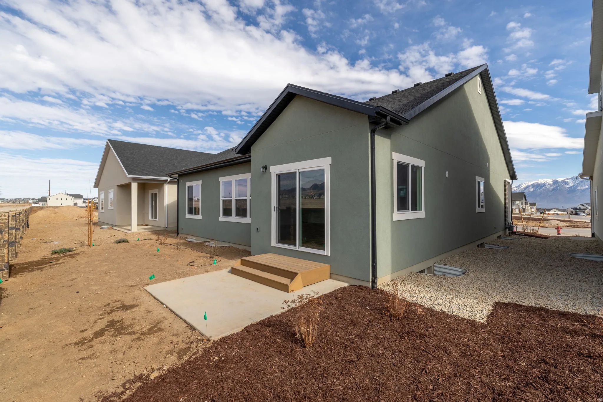 Rear exterior with stucco siding, asphalt shingle roofing, multiple windows, a concrete patio, and wooden steps