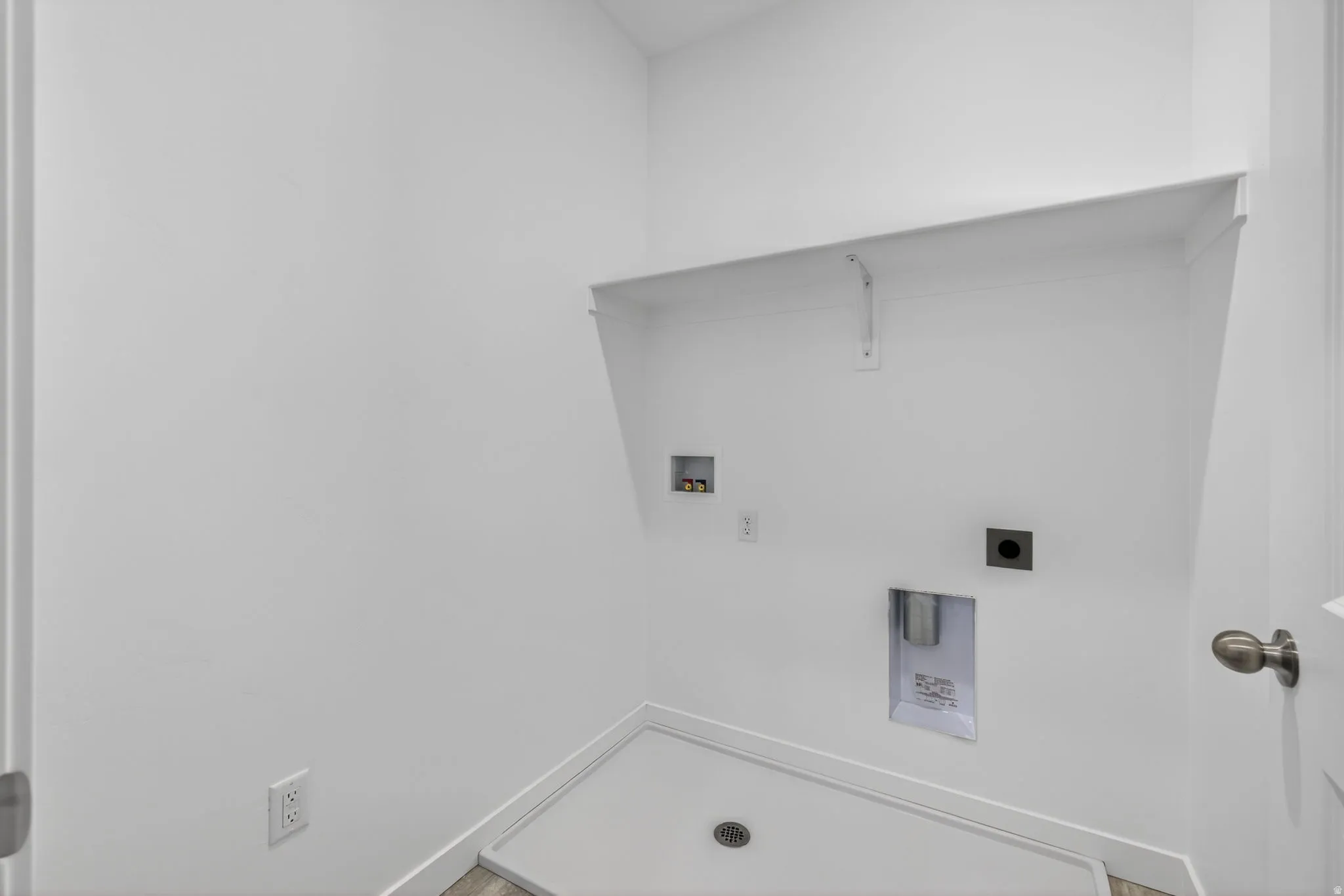 Dedicated utility space featuring a built-in shelf, appliance hookups, and a floor drain