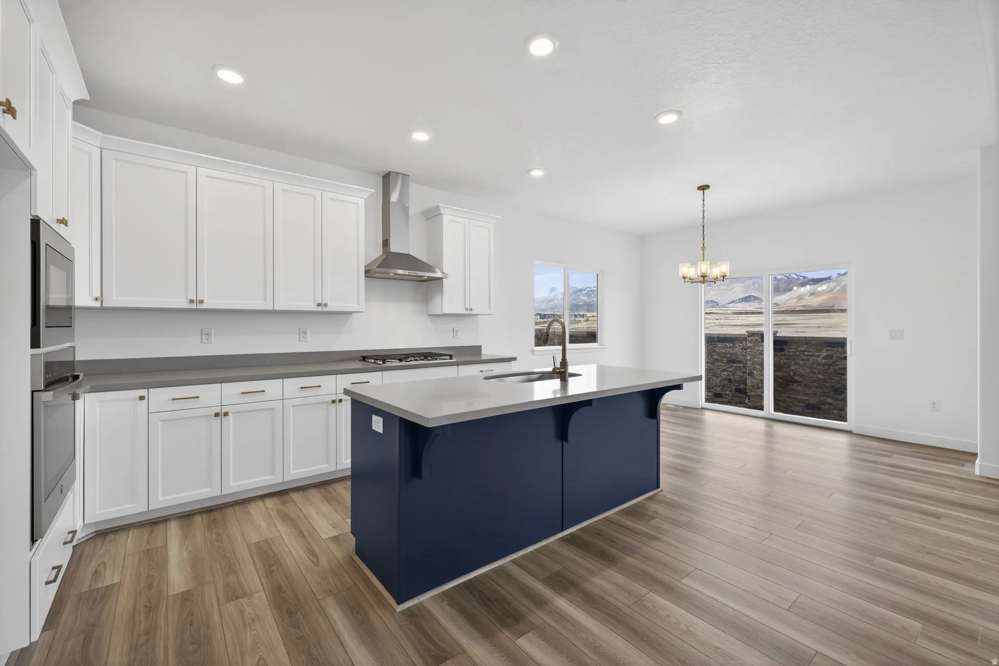 Kitchen featuring white cabinetry, a blue central island, integrated stainless steel appliances, wood-finish flooring, and recessed lighting