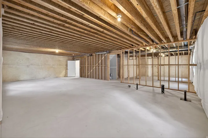 Unfinished basement with exposed wood joists, concrete flooring, and partial wood framing for future development