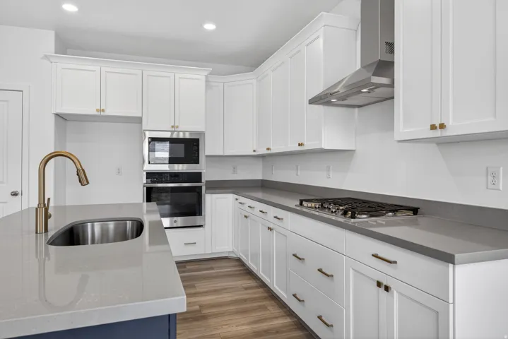 White cabinetry with gold-tone hardware, stainless steel appliances, solid surface countertops, and wood-finish flooring