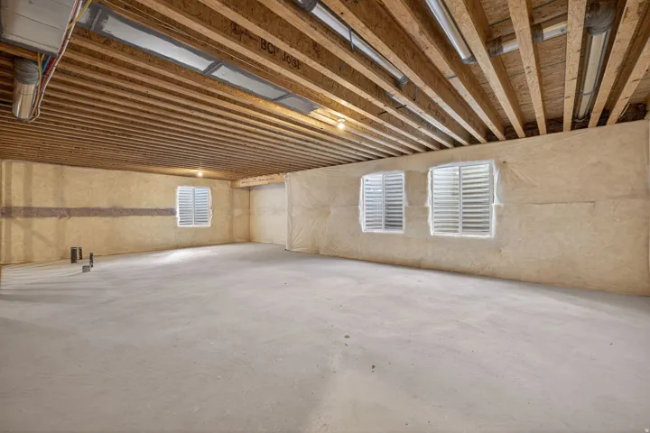 Unfinished basement with exposed ceiling joists, concrete flooring, and multiple window openings