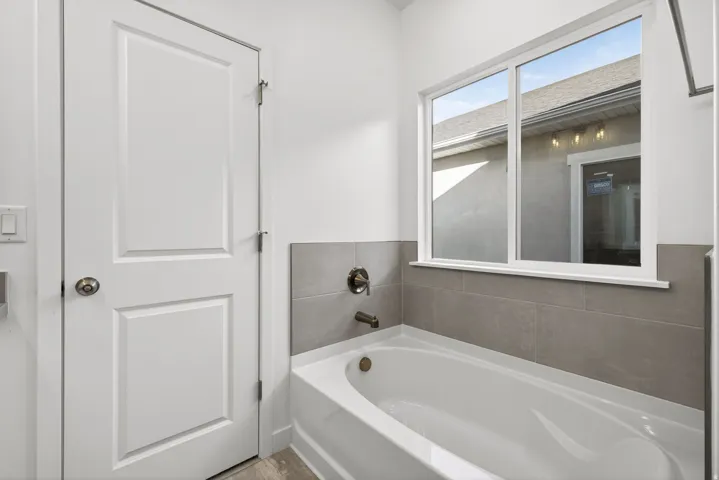Bathtub with gray tiled surround, bronze-finish fixtures, and a large window