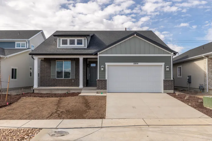 Contemporary ranch-style exterior featuring a covered entry, dark brick accents, light green siding, a two-car garage, and a concrete driveway