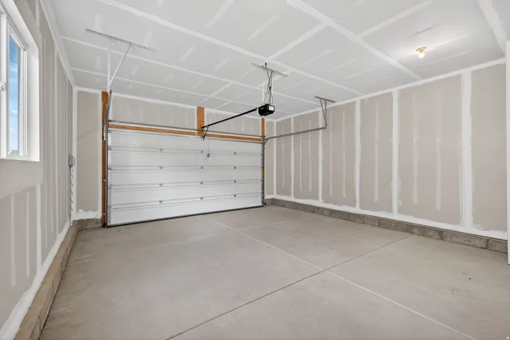 Spacious garage with an automatic overhead door, concrete flooring, window, and overhead lighting