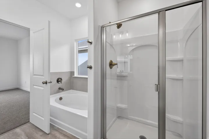 Bathtub and shower combination featuring a glass enclosure, tiled surround, and brushed bronze fixtures