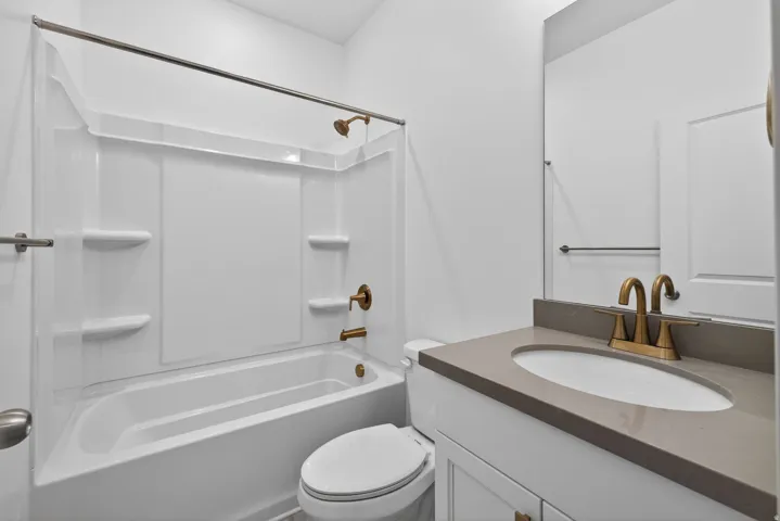 Bathroom featuring a white integrated tub and shower unit, bronze-finish fixtures, a vanity with a rectangular sink, and a gray countertop