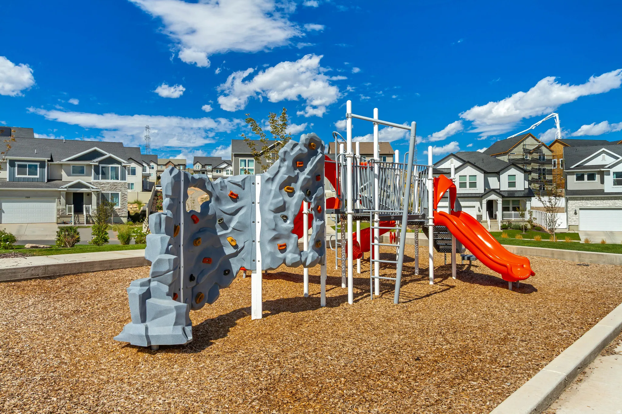 Community playground with a rock climbing wall, slide, and wood chip ground cover