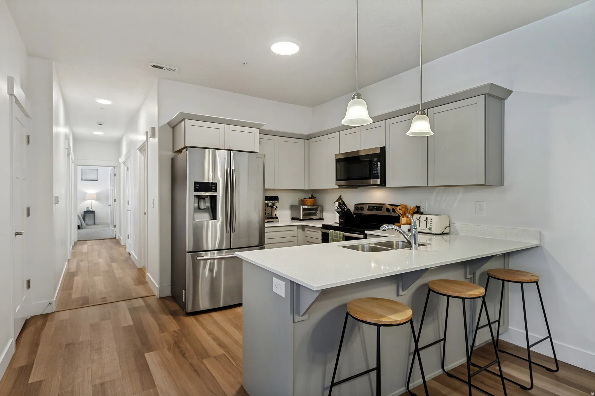 The kitchen features stainless steel appliances, light-toned cabinetry, quartz countertops, and a breakfast bar
