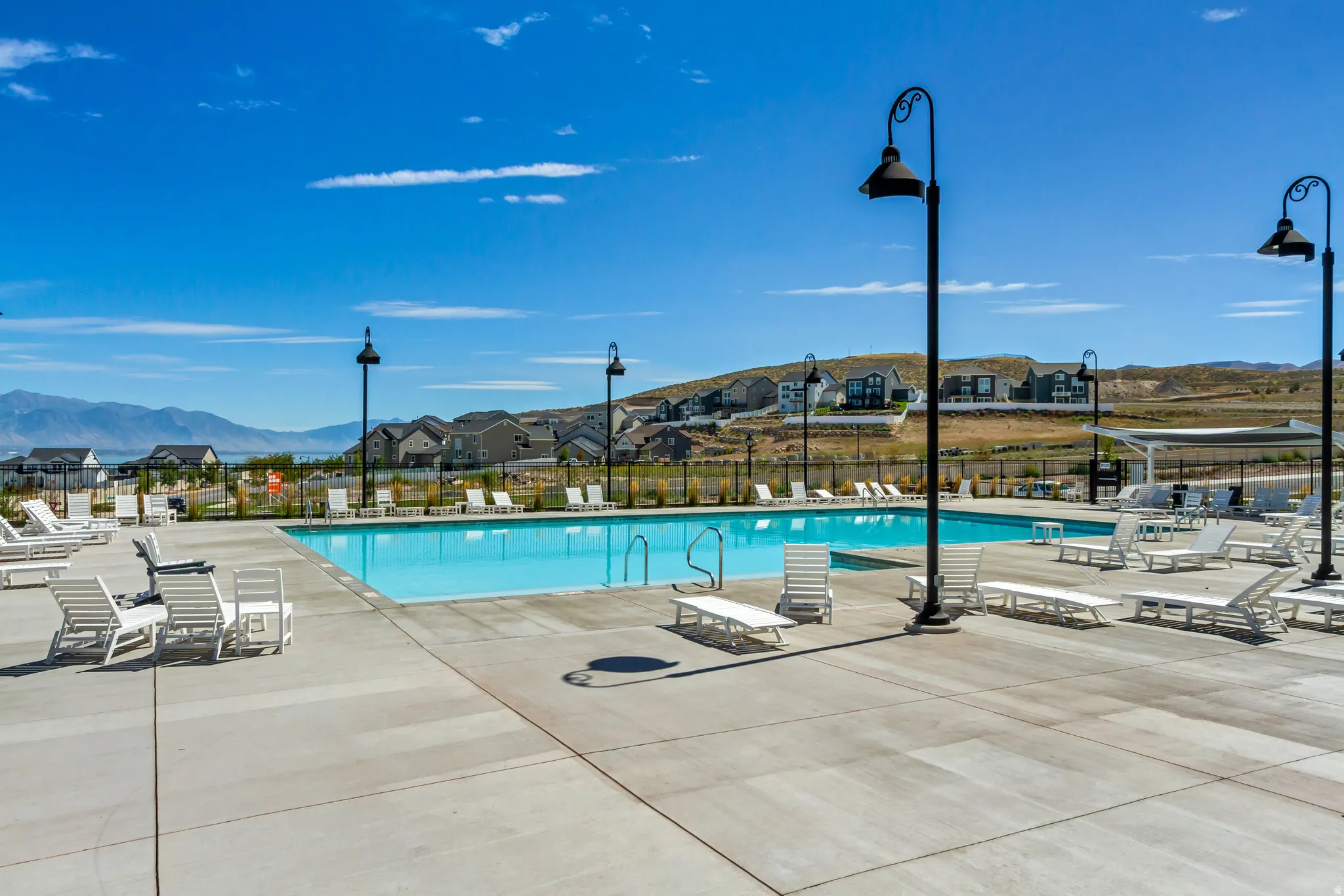 Expansive outdoor swimming pool with surrounding concrete decking, complemented by decorative streetlights and a mountain landscape