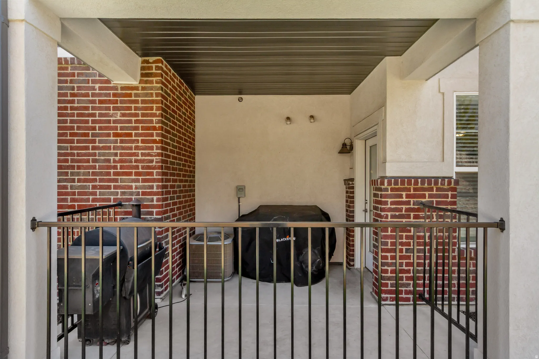 Covered outdoor patio with a bronze-finish railing, brick siding, and stucco walls